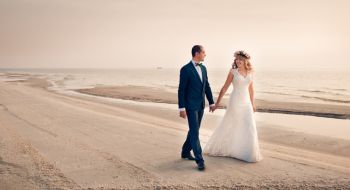 a bride and groom walk hand in hand on the beach
